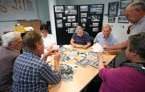 Cette photo représente les archives municipales. On retruove 7 personnes autour d'une table en train de trier des photos en noir et blanc