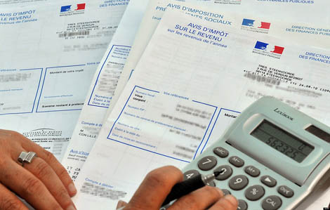Cette photo illustre les impôts. Elle représente des feuilles d'impôts, une calculatrice ainsi qu'une personne qui les remplis