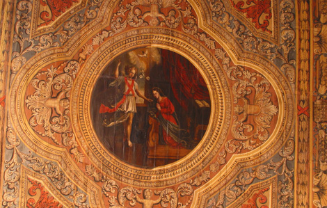 Cette photo représente le plafond de la chapelle Saint Benoît. Il est constitué de lambris en bois. Il est divisé en trois panneaux, bordés de panneaux rectangulaires plus petits. Sa référence est le mystère de la Vierge.