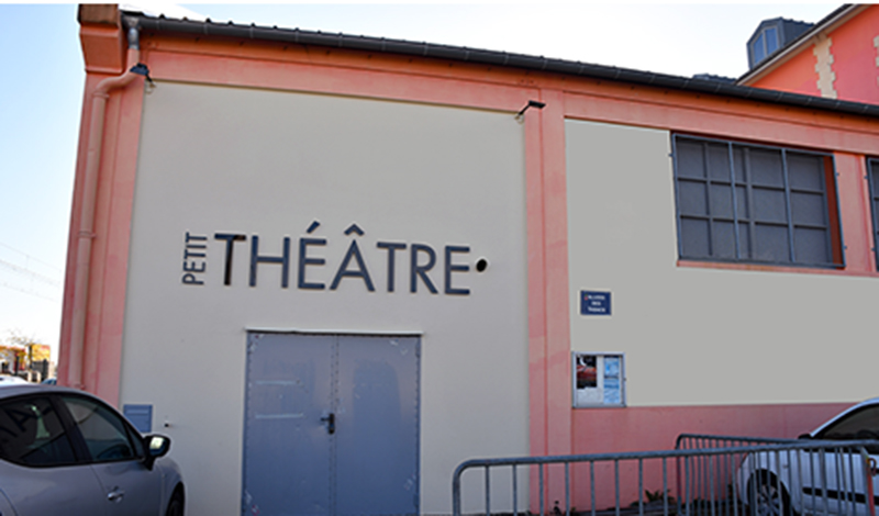 Cette photo représente le petit théâtre Coluche. La couleur dominante de cette image est le orange des bâtiments. Une voiture est garée devant le Petit Théâtre