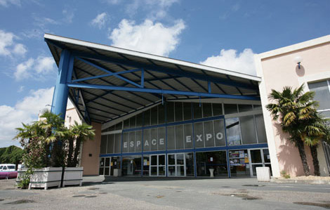 Cette photo représente la façade extérieure de l'espace des expositions de Marmande. On retrouve son avant toit triangulaire ainsi que son poteau de soutient bleu