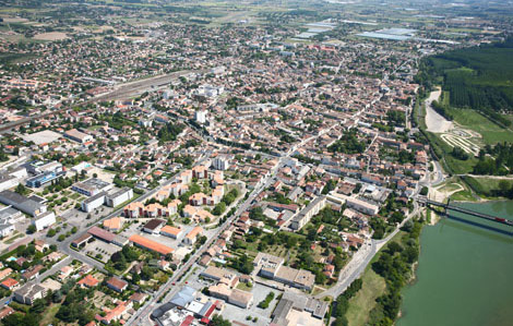 Photo représentant Marmande vu du ciel. Cette photo est une vue aérienne de Marmande. On a à droite le pont de Marmande et la Garonne, à gauche on a la ville de Marmande