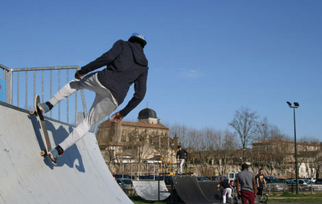 Cette photo représente un jeune portant une casquette grise et une veste à capuche noire faisant du skate au skate park de Marmande. D'autre jeunes sont présents et s'amusent