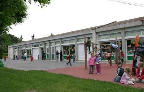 Cette photo représente une cours d'école. Des enfants jouent sur diverses installations de jeux, d'autre sont assis.